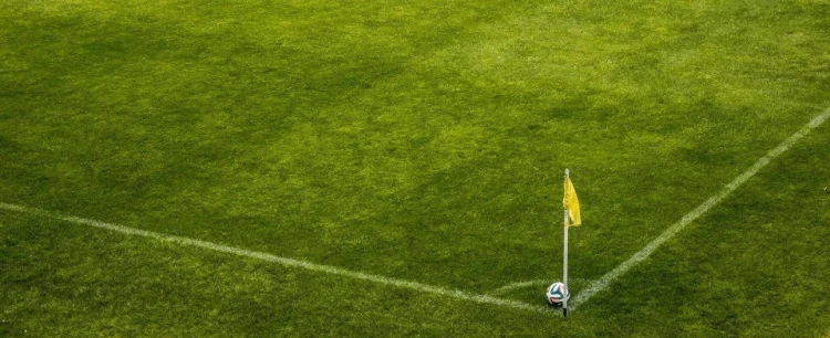 Esquina de una cancha de fútbol, con una bandera amarilla y una pelota.